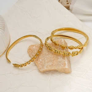 Tre bracciali in acciaio al titanio dorato con zirconi in design a V, conchiglia e maglia U