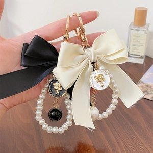Elegant satin bow keychain with faux pearl strings and golden charms on wooden surface