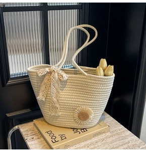 Detail of hand-woven off-white tote bag with lace bow and sunflower accent on a book