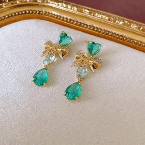 Boucles d'oreilles nœud vintage avec cœur vert et cristaux goutte sur fond texturé