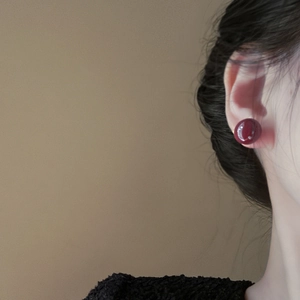 Close-up of deep burgundy red round stud earrings with high-gloss finish on a model