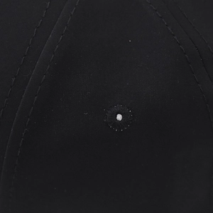 Detail view of reinforced stitching and embroidered eyelet on a black baseball cap fabric