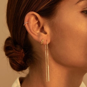Close-up of gold chain earrings and purple zircon ear cuff on model with soft lighting