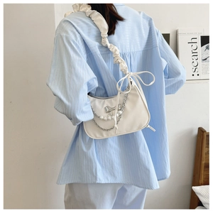 Detail of white cloud underarm bag with silver bow charm and pearl chain accent