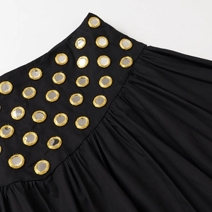 Détail de tissu noir avec broderie d'œillets miroir dorés et coutures fines
