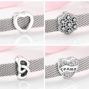 Macro detail of S925 sterling silver heart and flower charms on a mesh bracelet