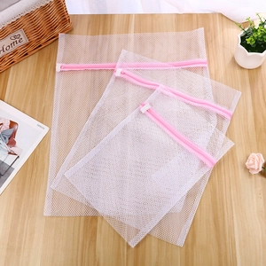 Three sizes of mesh laundry bags with pink zippers on a wooden table for clothes care