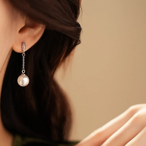 Detail of long drop pearl earring with zircon chain worn by a model in soft lighting