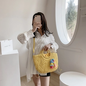 Detail of yellow woven straw bag with colorful tassel and drawstring closure