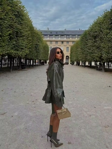 Street style shot of a dark green leather jacket with waist belt and a beige handbag