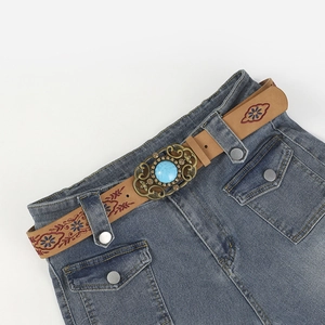 Close-up of brown leather belt with embroidery and turquoise buckle on denim skirt
