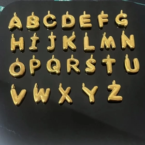 Macro view of 26 golden 3D puffy alphabet pendants arranged on a reflective black background