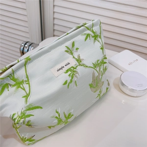 Détail de la broderie florale verte et de l'étiquette en tissu sur la trousse de maquillage
