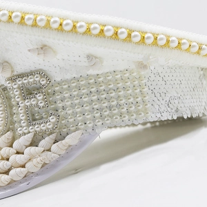 Macro shot of white sequin hat featuring a pearl letter E and natural sea shells