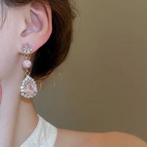 Close-up of pink teardrop dangle earrings with sparkling stones on a model's ear