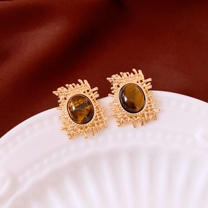 Close-up of vintage oval tiger eye earrings with golden woven texture on a ceramic plate