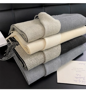 Close-up of four thick cashmere blend scarves with tassels folded on a leather sofa