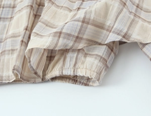 Detailed view of elastic cuffs on a plaid cropped top with beige and brown cotton texture