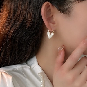 Vue détaillée d'une boucle d'oreille dorée avec pendentif cœur blanc porté à l'oreille