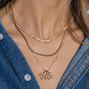 Close-up of triple layered gold-plated necklaces with BAJ initial pendants on model