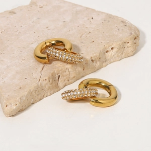 Detailed macro of gold double hoop earrings with cubic zirconia on beige stone base