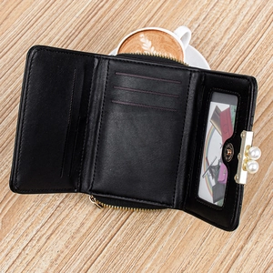 Interior detail of a black tri-fold wallet showing card slots and pearl clasp on wood