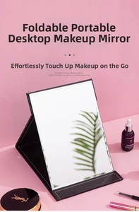 Close-up of the black foldable portable desktop makeup mirror on a pink surface.