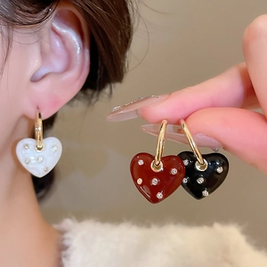 Close-up of heart-shaped drop earrings in red, black, and white with diamond accents