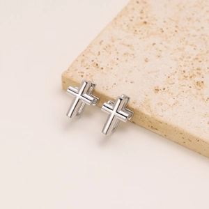 Macro shot of silver cross hoop earrings in stainless steel on a beige stone surface