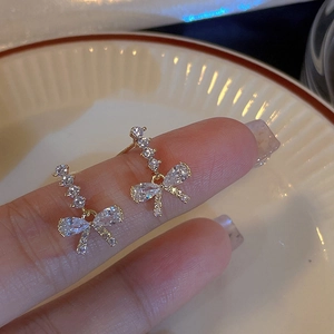 Elegant sparkling bow knot stud earrings with zircon stones and golden finish on a hand