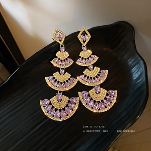 Elegant gold fan-shaped drop earrings with purple rhinestones on black display