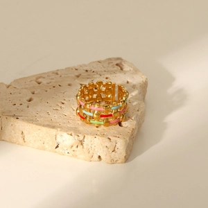Detailed macro view of hollow mesh 18K gold ring with multi-color enamel on beige stone