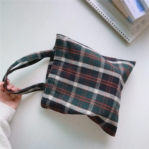 Draufsicht auf eine Vintage-Pläd-Canvas-Tasche auf einem weißen Holztisch mit Büchern