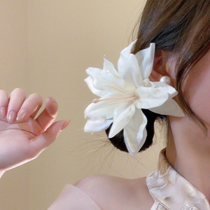 Close-up of a white fabric lily hair clip with pearl detailing worn by a model