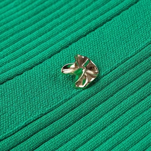 Détail macro d'un bouton doré ondulé sur une robe en maille côtelée vert foncé