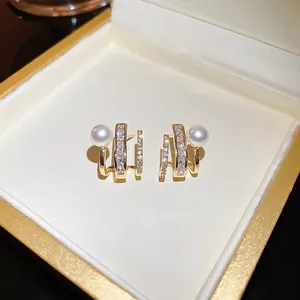 Elegant gold-plated claw earrings with layered zircon pavé and white pearls on jewelry box