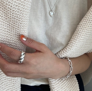 Close-up of minimalist silver heart necklace, spiral ring and link bracelet on model