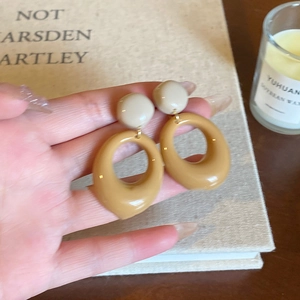 Close-up of vintage caramel resin hoop earrings held by hand over lifestyle props