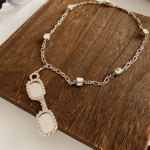 Detail of silver necklace with lorgnette pendant and square zircons on wood
