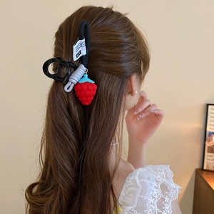 Detail view of a cute red strawberry hair clip worn on long wavy hair with HY logo tag