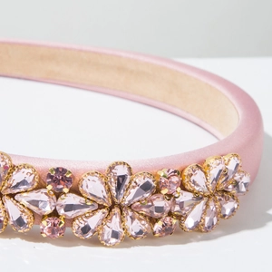 Makrodetail eines rosa Satin-Hairreifs mit Kristallblumenmuster und Goldmetallkrallen
