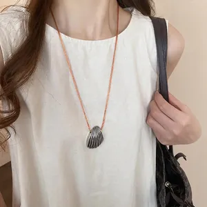 Silver shell pendant necklace with brown cord cord on model in warm aesthetic