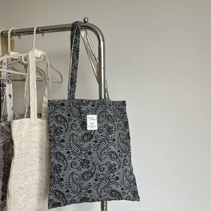 Detail of grey canvas tote bag featuring classic white paisley patterns and minimalist patch