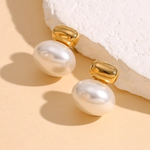 Macro shot of gold-plated stud earring with a large white oval pearl on textured stone