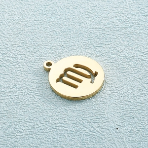 Macro detail of a golden Virgo zodiac sign circular pendant on a light blue background