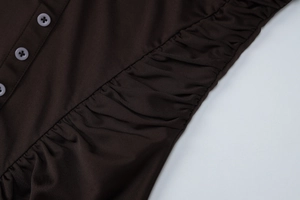Detalle de vestido marrón oscuro con pliegues texturizados y botones clásicos