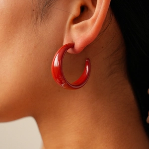 Close-up detail of glossy dark red C-shaped hoop earrings with a high-shine polished finish