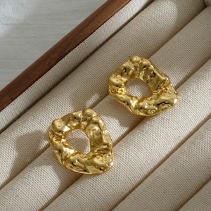 Macro detail of irregular gold hoop earrings with hammered metal lava texture