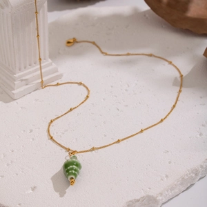 Detailed macro view of a gold beaded chain with a green conch shell pendant