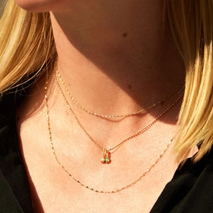 Close-up of layered gold titanium necklaces featuring a birthstone pendant and rope chain